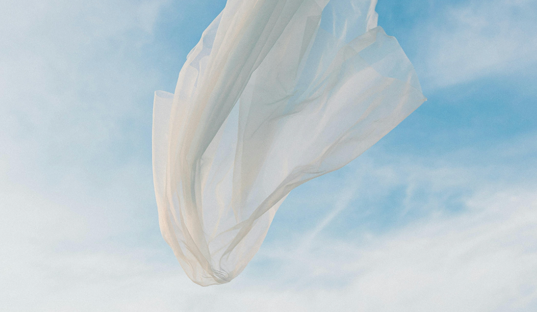Sheer white fabric billowing gently in a bright blue sky